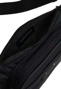 Schwarze Umhängetasche aus Nylon mit Reißverschluss und Außentaschen, innen mit Logolabel und verstellbarem Riemen.