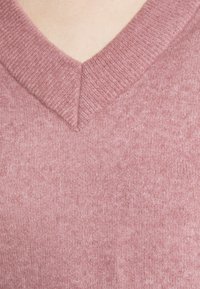 V-ringad tröja i ett mjukt, texturerat ljust rosa stickat material. Har en ribbad krage och jämn sömnad genom hela plagget.