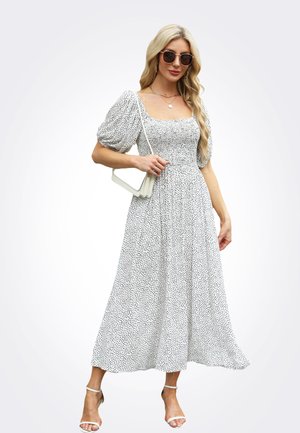 Vestido blanco con lunares negros, escote cuadrado y mangas abullonadas. Diseño vaporoso de longitud media combinado con sandalias de tacón bloque transparente.