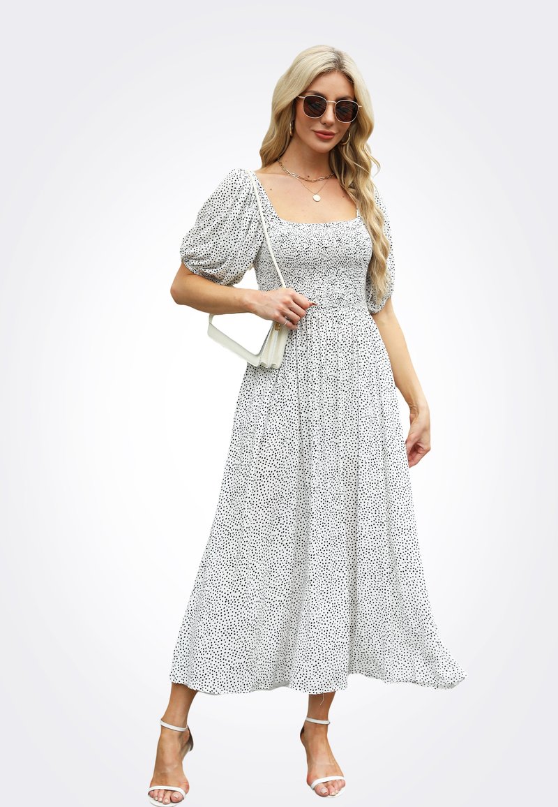 Vestido blanco con lunares negros, escote cuadrado y mangas abullonadas. Diseño vaporoso de longitud media combinado con sandalias de tacón bloque transparente.
