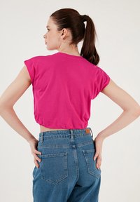 Kort lyserød cropped T-shirt med cap sleeves, let struktureret stof, parret med højtaljede blå denimjeans med et lædermærke bagpå.