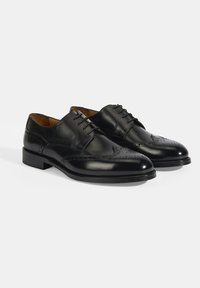 Zwarte leren dresschoenen met een gladde afwerking, teenkap met perforaties en een lage gestapelde hak. Klassiek veterschoenontwerp met gedetailleerde stiksels.