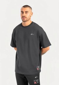 Dark gray oversized t-shirt made of cotton blend, featuring a crew neck, short sleeves, and a small logo on the chest with label accents.