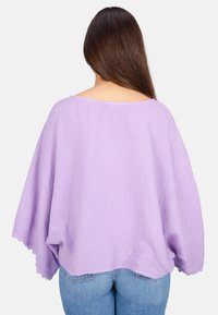 Oversized-Lavendeloberteil aus strukturiertem Stoff mit losem Sitz und gewelltem Saum. Die Ärmel hängen seitlich herab und das Oberteil hat einen weiten Ausschnitt.