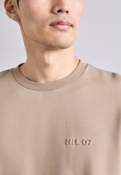 Beige-siniseg, ümmarguse kaelusega, pehme tekstuuriga ja rinnal kõrgtrükitud logo "NN. 07". Lihtne, kaasaegne disain ribaga kaelas.