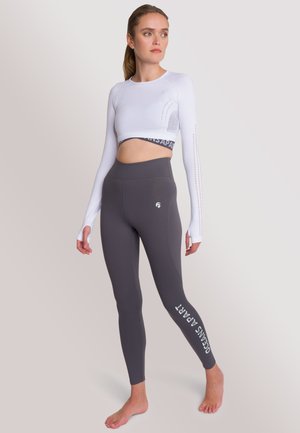 Witte lange mouwen cropped top met een mesh-design en grijze high-waisted leggings met de tekst "OCEANS APART" in het wit. Soepele stofstructuur.