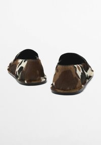 Brown and white patterned slip-on shoes made of soft fur with a matte black sole and open back design.