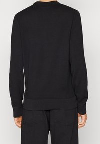 Černý pletený svetr s žebrovaným kulatým výstřihem a lemem. Má dlouhé rukávy a strukturovaný povrch, vhodný pro každodenní nošení.