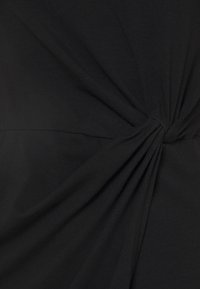 Svart t-shirt med en snodd detalj på sidan, tillverkad av mjukt, stretchy tyg med en slät yta.