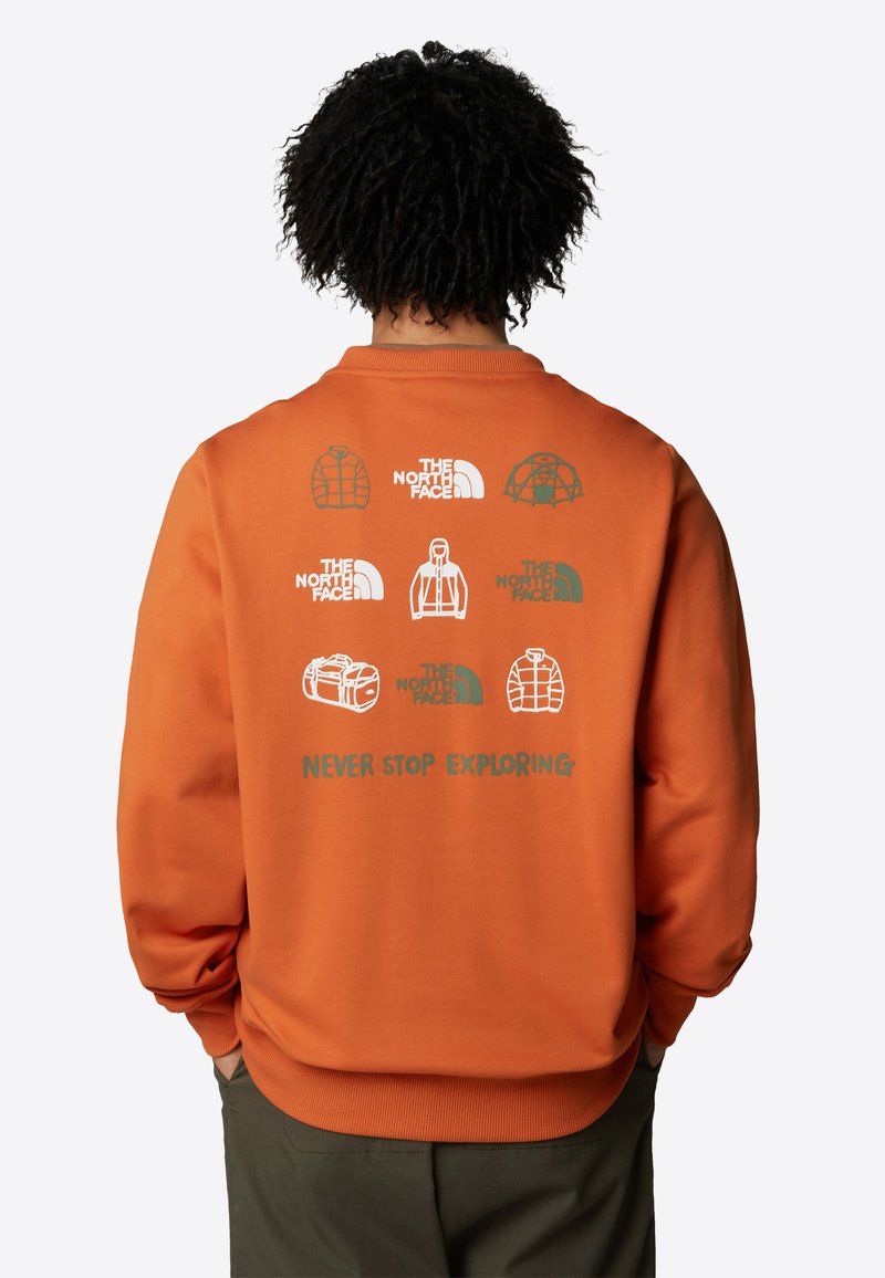 Orange sweatshirt med olika logotyper från The North Face på baksidan. Texten lyder "NEVER STOP EXPLORING" i grönt. Mjuk, strukturerad textil.