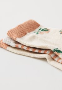 Calzini a fantasia impilati, con una base di crema chiara, accenti pesca, design floreali e un maglione testurizzato, con un polsino a righe in corallo e bianco.