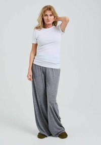 Vit kortärmad t-shirt ihop med lösa grå pyjamasbyxor. Mjukt tyg, avslappnad passform och platta gröna tofflor. Enkel, avslappnad hemmaklädsel.