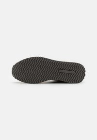 Sole di scarpa in gomma nera con un motivo di battistrada ondulato. Presenta il nome del marchio impresso al centro e un bordo curvo per una maggiore flessibilità.