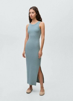 Un lungo abito aderente in morbido tessuto blu con scollo rotondo e spacco laterale. La modella lo abbina a scarpe espadrillas color cammello.