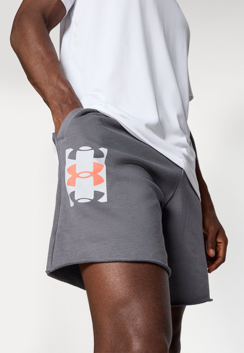 Graue Sportshorts mit einer strukturierten Oberfläche. Auf dem linken Bein befindet sich ein weißes und oranges Under Armour-Logo. Dazu wird ein weißes T-Shirt kombiniert.