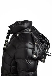 Schwarze Daunenjacke mit hohem Kragen, Druckknöpfen und verstellbarem Tragegurt mit dem Aufdruck "JACK1T" auf weißem Hintergrund.