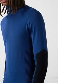 Top a maniche lunghe blu reale, con accenti neri testurizzati e strisce orizzontali sui lati. Tessuto liscio con collo alto.