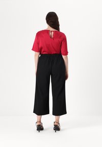 Punane satiinist pluus tagant lipsuga, koos mustade laia säärega pükstega. Riietus on lõdva istuvuse ja kontrastsete tekstuuridega.