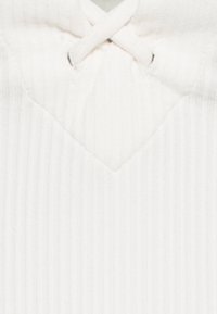 Vitt ribbat tyg med en V-formad halsringning och en intrikat snörningsdetalj i mitten. Texturen verkar mjuk och något elastisk.