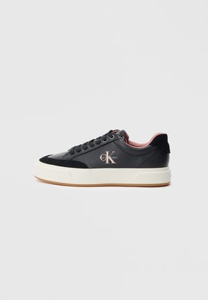 Zapatilla negra de caña baja con suela blanca gruesa, cordones negros y forro interior rosa, con el logo de Calvin Klein en el lateral.