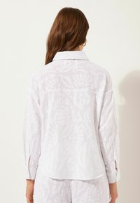 Camicia bianca con un motivo floreale testurizzato, collo e polsini bottonati. Vestibilità ampia con spacchi laterali; tessuto leggero.