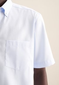 Camicetta azzurra a maniche corte realizzata in tessuto texturizzato, con colletto a punta e una tasca sul petto.