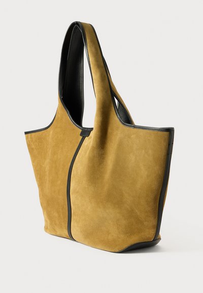 Žuta suede torba s crnim kožnim detaljima, koja ima široko otvaranje i mekanu teksturu. Zaobljenog, izduženog oblika s minimalnim hardverom.
