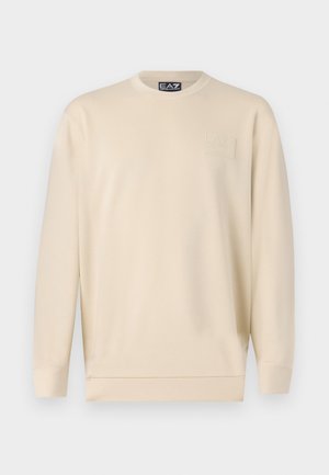 Beige sweatshirt made of soft, lightweight fabric. Features a crew neckline and a small logo patch on the left chest. Simple design.