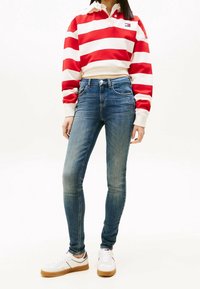 Rood-wit gestreepte lange mouwen polo met een kraag, gedragen met donkerblauwe skinny jeans en witte sneakers met een tan zool.