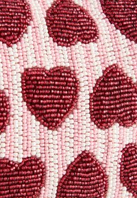 Gyöngyökkel ékesített szövet, piros szívformákkal rózsaszín és fehér háttéren, változó gyöngytextúrákkal és színekkel, amelyek térhatású látványt keltenek.