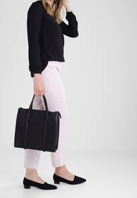 Zwarte leren tote bag met een gestructureerd ontwerp, twee bovenhandvaten en contrasterende zijnaad. Gemaakt met lichtroze broeken en zwarte flats.
