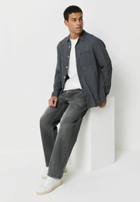 Czarna i biała koszula w kratę na białej koszulce, połączona z szarymi prostymi dżinsami i białymi trampkami, siedząca na białym piedestale.