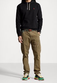 Svart huvtröja med dragsko, khaki cargobyxor med fickor, och flerfärgade sneakers med vita snören och gröna detaljer.