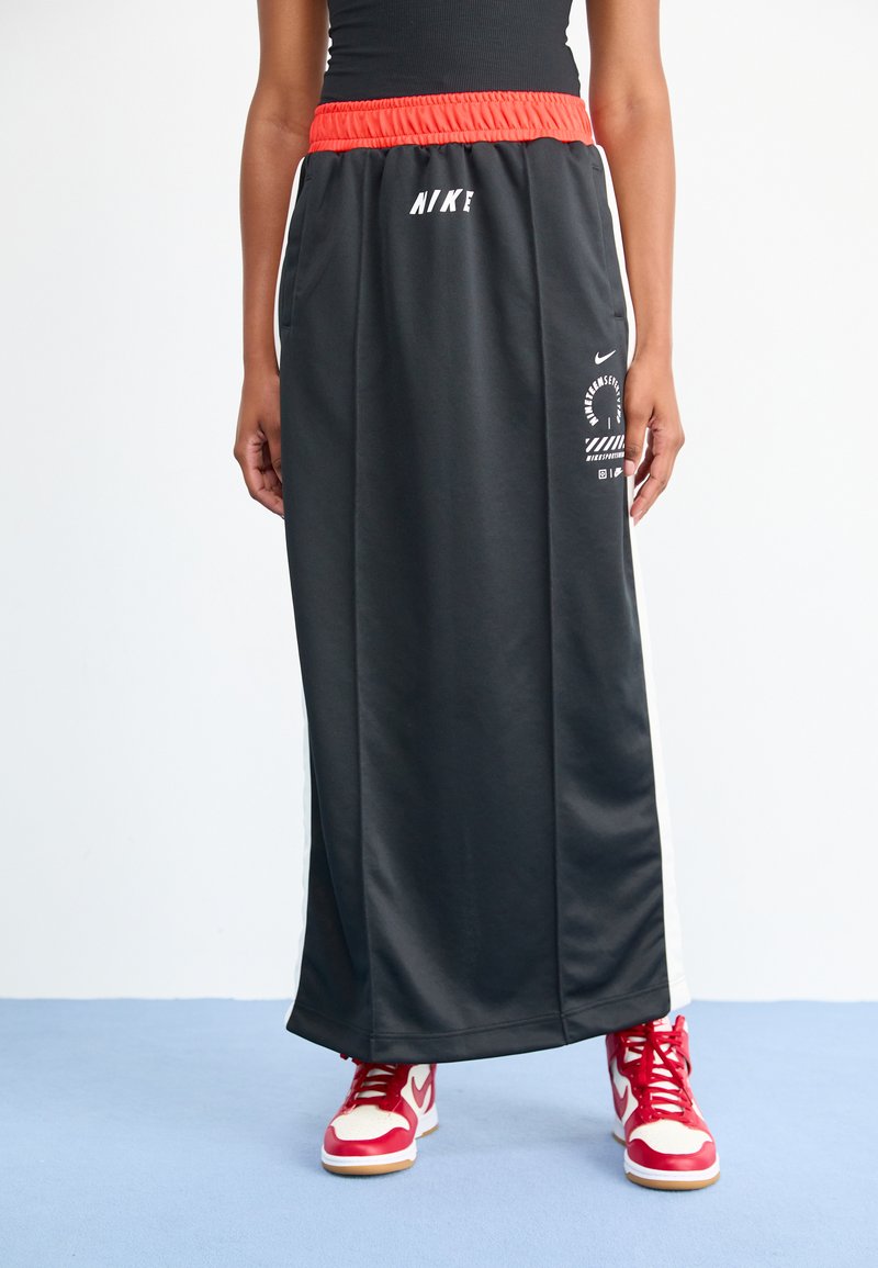 Falda atlética negra con una cinturilla elástica roja, que presenta franjas laterales y un estampado gráfico. Combinada con zapatillas rojas y blancas.