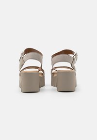 Beige platform sandals with an open back, suede upper, and a thick, textured sole. Adjustable ankle strap with a silver buckle accent.
