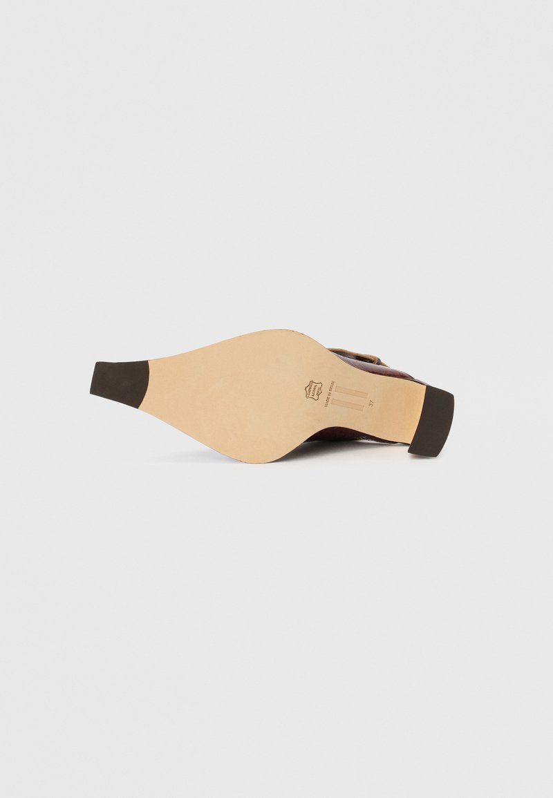 Suela de zapato de cuero con un diseño curvado, color marrón claro con textura lisa, y una tapa de tacón de goma oscura en contraste.