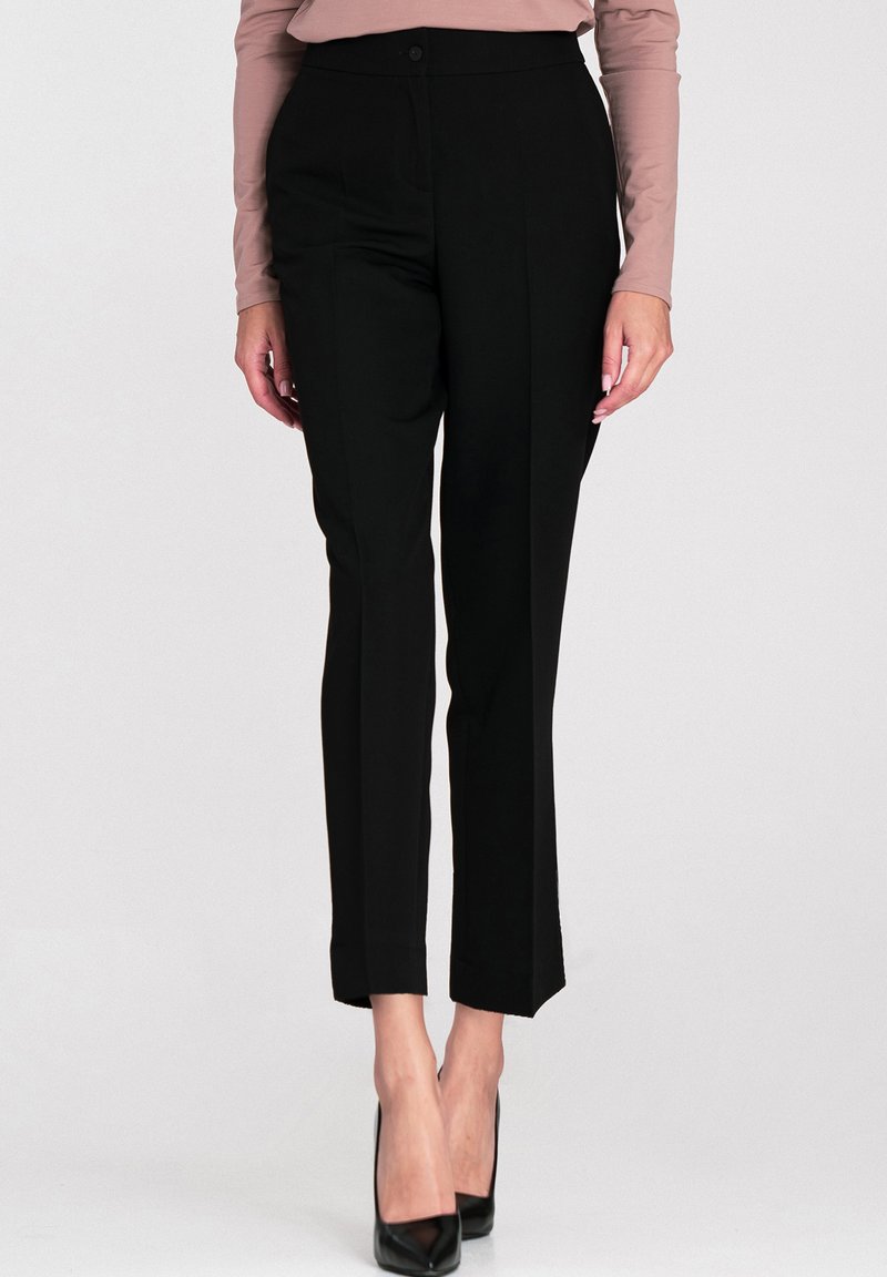 Czarne spodnie o dopasowanym kroju, z zapięciem na guzik i detalami w postaci zakładek, zestawione z butami na obcasie.