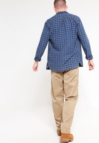 Navy geblokte lange mouwen shirt met een kraag, gecombineerd met beige broeken en bruine laarzen. De stof lijkt zacht en heeft een relaxed fit.