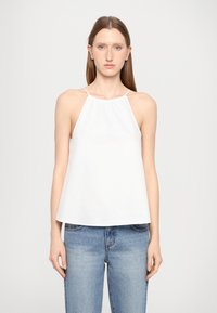Weißes Top mit Trägern und gerafftem Dekolleté, aus weichem Stoff, lockere Passform und dünne Träger, kombiniert mit hellblauen Jeans.