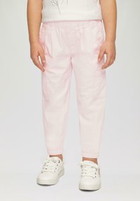 Pantalons cargo pour enfants de couleur rose clair avec des poignets élastiques, des poches latérales et une coupe décontractée, associés à des baskets blanches. Tissu en coton doux.