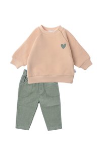 Peach sweatshirt with a green heart print, paired with ribbed green corduroy pants featuring side pockets and an elastic waistband.
