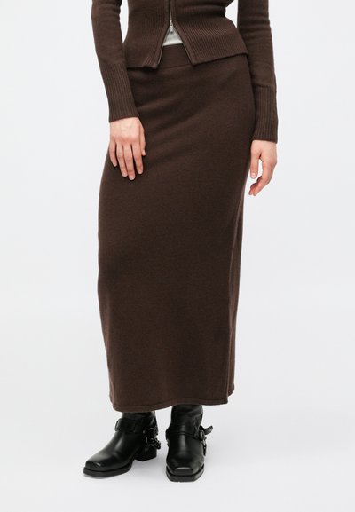 Brown, knit, mid-length skirt with a smooth texture. Worn with black ankle boots featuring buckle accents. Simple, minimal design.