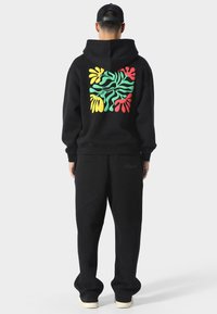 Sudadera con capucha negra con un diseño abstracto colorido en la parte posterior, combinada con pantalones de chándal negros y zapatillas blancas.