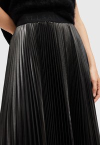 Black pleated skirt featuring a textured fabric, with an elastic waistband displaying the brand name "ALLSAINTS" embossed.