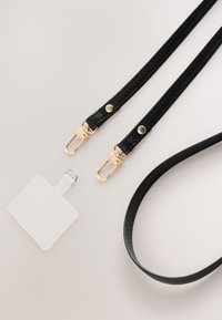 Schwarzes Lederband mit strukturierter Oberfläche, goldenen Metallklammern, zwei Druckknöpfen und einem kleinen weißen Etikett mit silberner Befestigung.