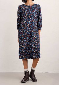 Vestido floral navy con mangas 3/4, que presenta un escote redondeado, detalle de botones y patrones de flores azules con acentos rojos. Lleva botas marrones.
