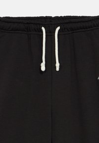 Zwarte sweatpants tailleband met witte trekkoorden die in eenvoudige knopen zijn gestrikt, tegen een plain achtergrond.