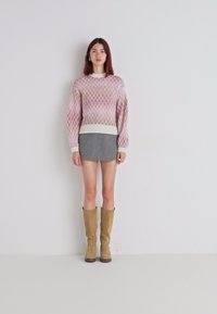 Lys rosa strikket genser med diamantmønster, kombinert med en grå miniskjørt og beige knelange støvler. Enkel, moderne design.