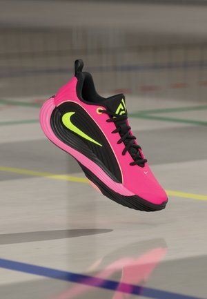 Φωτεινά ροζ και μαύρο αθλητικό παπούτσι Nike με νέον κίτρινο λογότυπο, μαύρα κορδόνια και λογότυπο, αιωρείται πάνω από το εσωτερικό γήπεδο με χρωματιστές γραμμές.
