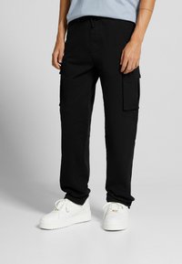 Svarta cargobyxor med avslappnad passform, med sidofickor och dragsko i midjan, kombinerat med vita sneakers för kontrast.